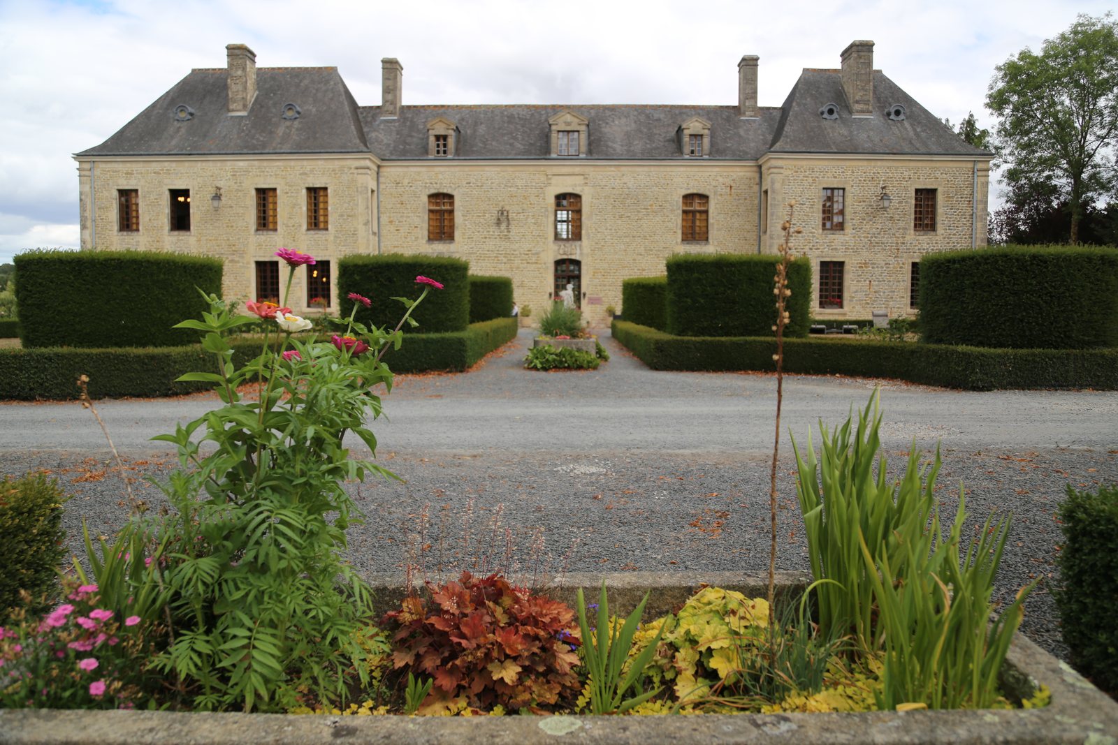 La façade et ses ifs, derrière le cercle de pierre fleuri